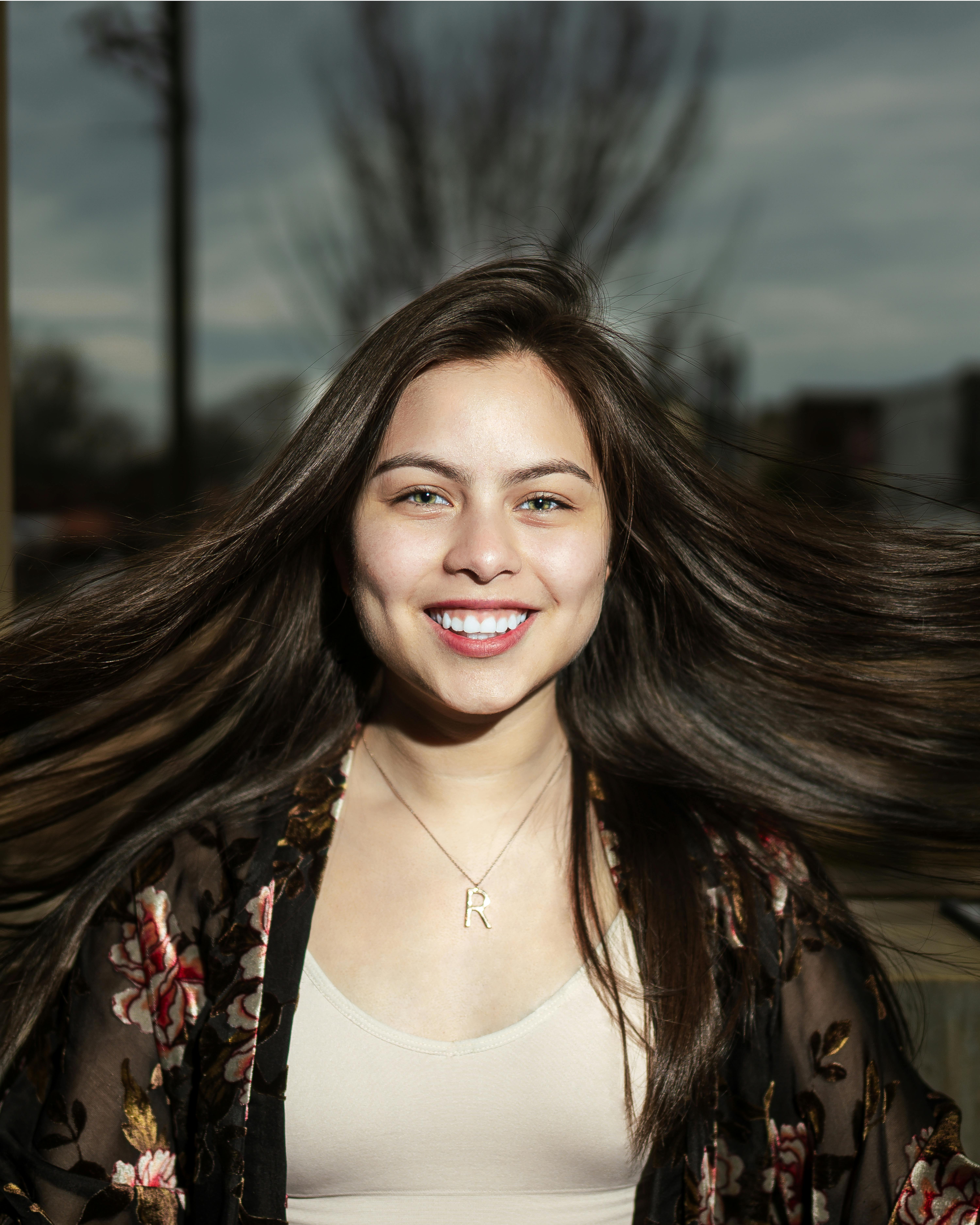 一位年轻女子微笑着，头发在风中飘扬，在自然光下被捕捉于户外