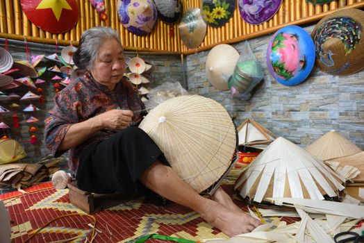 Elderly woman skillfully creating a traditional Vietnamese conical hat indoors.