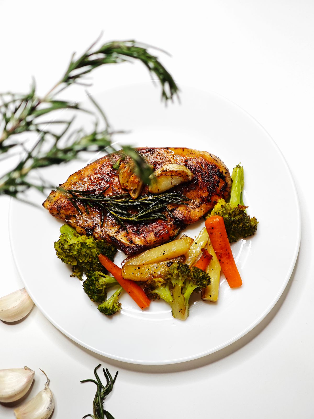 Roast chicken with rosemary and mixed vegetables on a white plate
