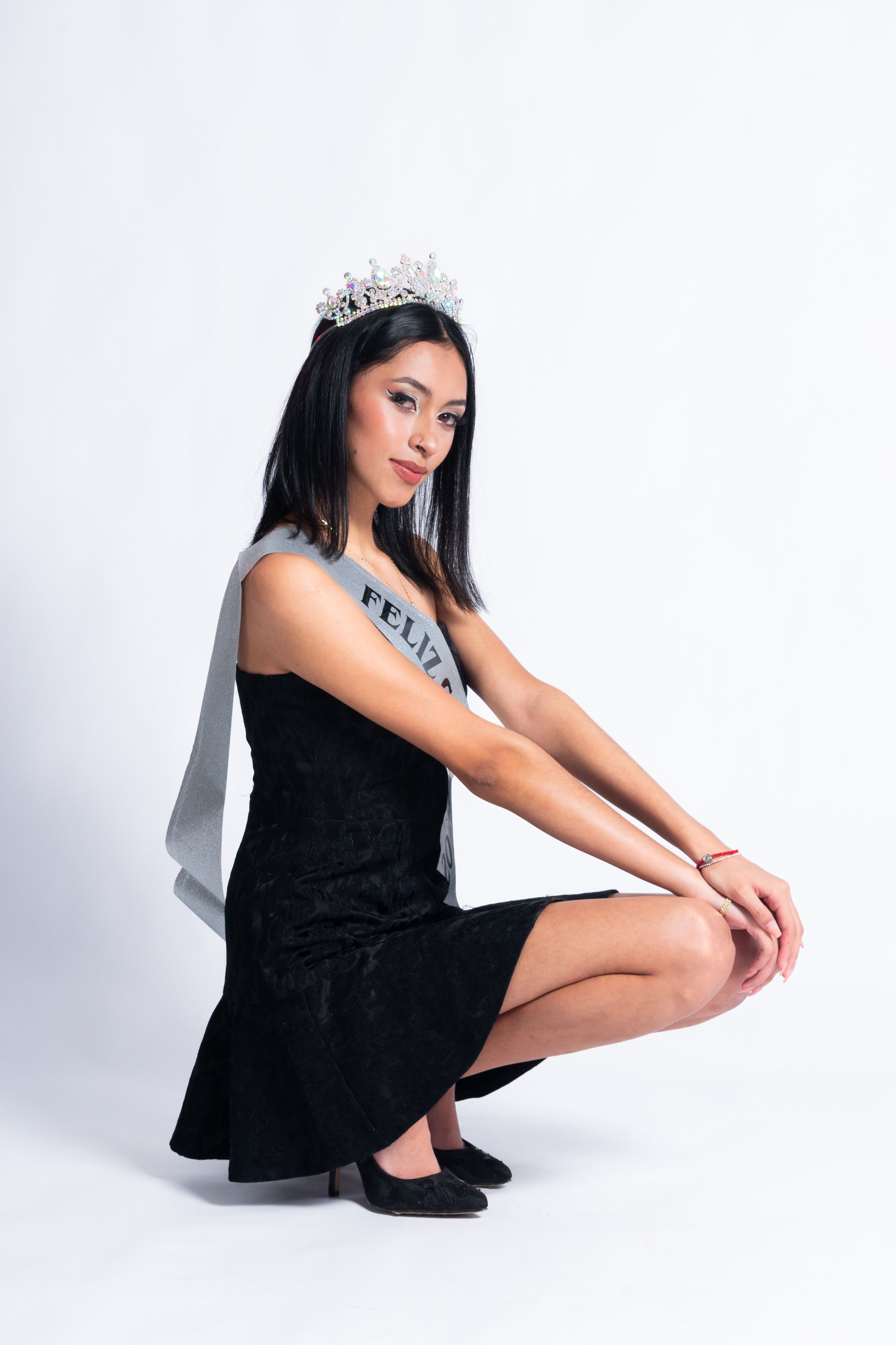 A graceful woman in black dress wearing a tiara and 'Feliz' sash for her birthday portrait.