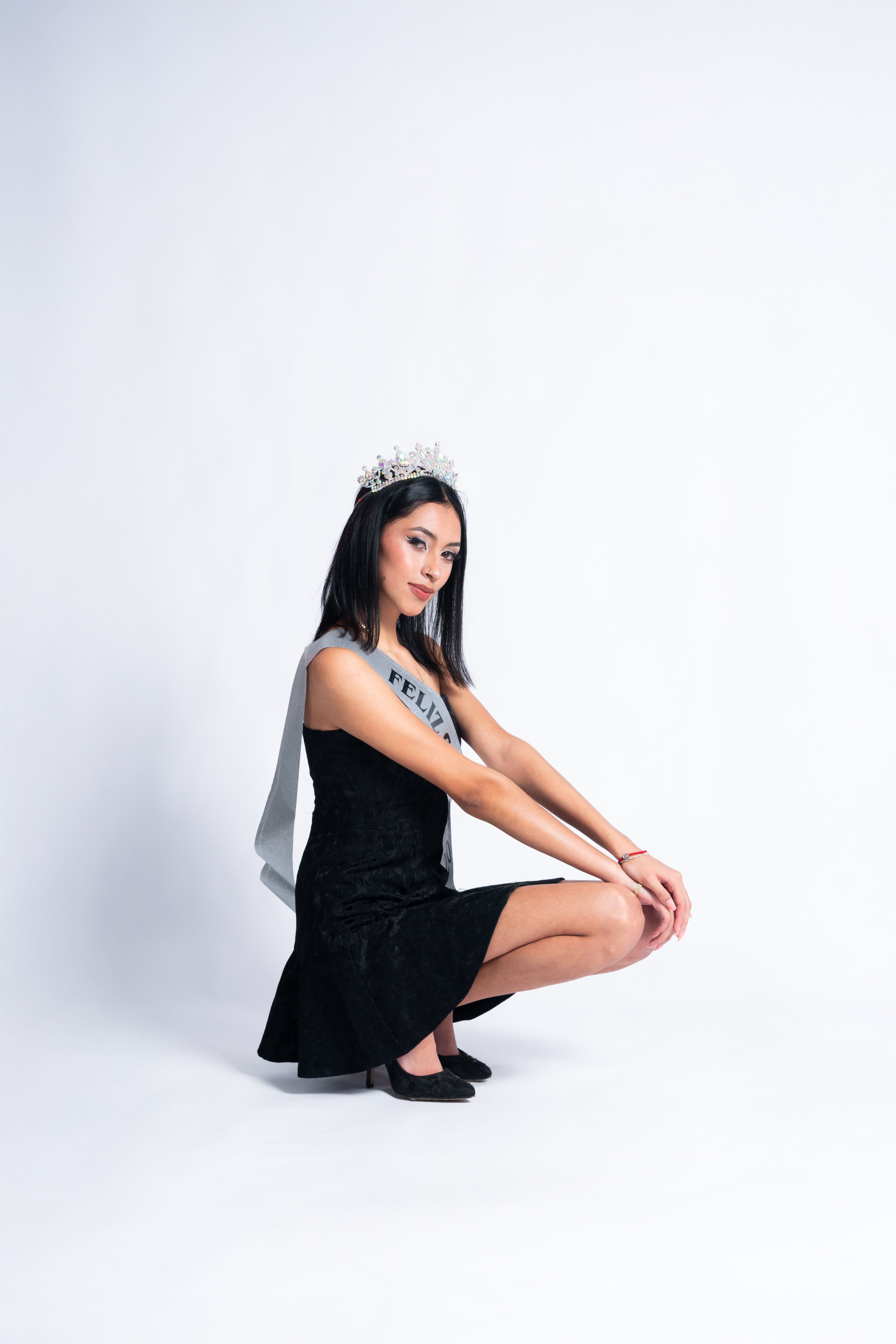 Stylish portrait of a woman celebrating her birthday wearing a tiara and sash in a studio setting.