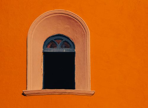 Free A vibrant arched window set against a bold orange wall, casting intriguing shadows. Stock Photo