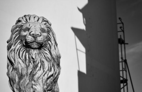 Black and white photo of a lion statue with building shadows, creating a dramatic effect.
