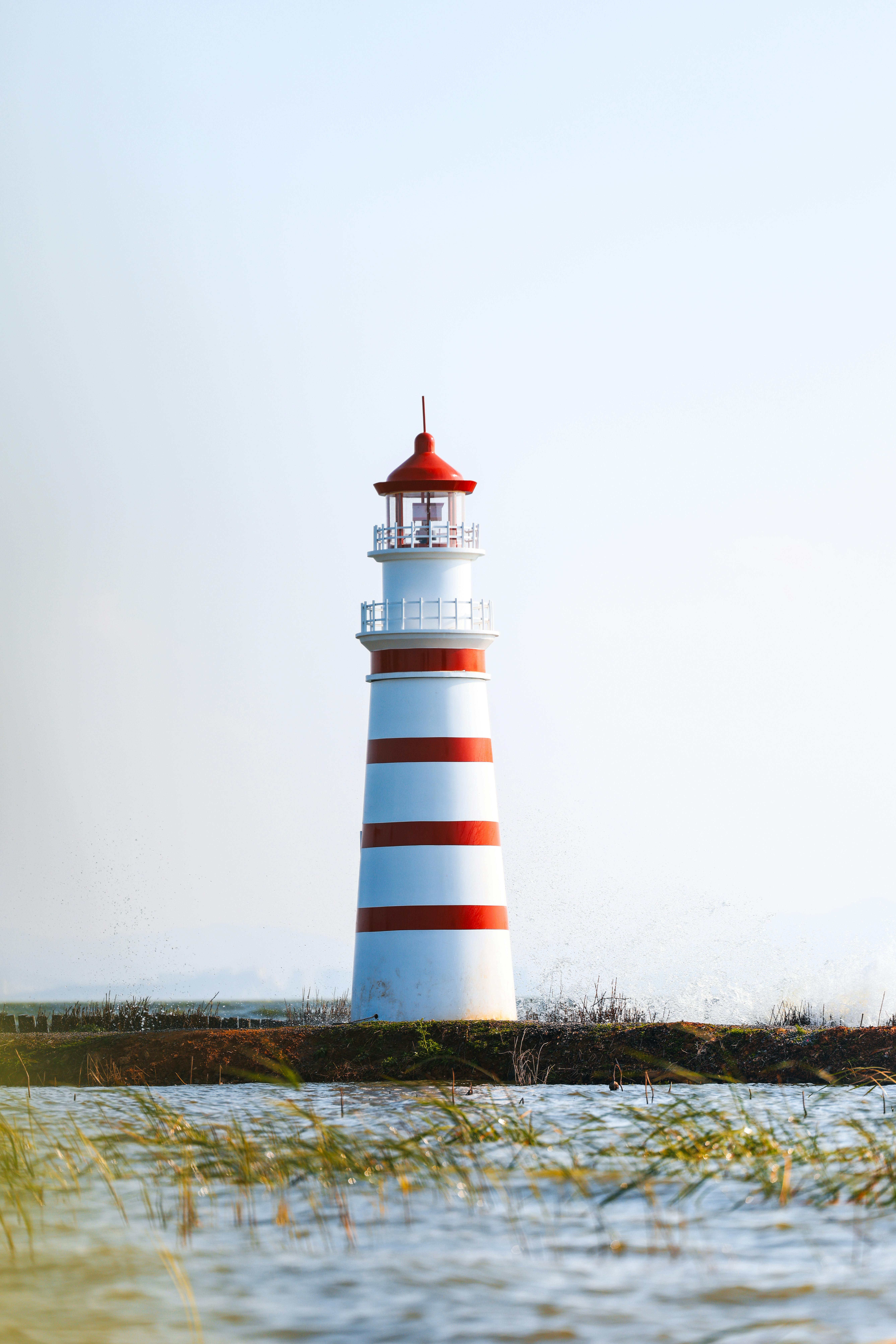 Free Vibrant lighthouse with red and white stripes standing tall by the calm sea, symbolizing guidance and safety. Stock Photo