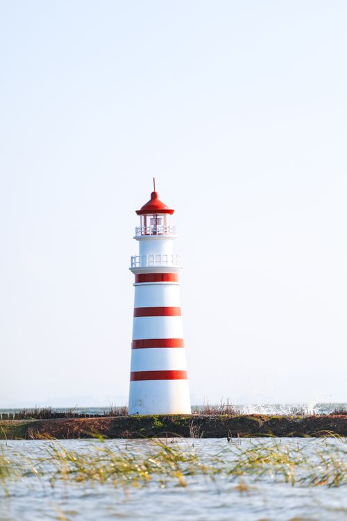 Free Iconic red and white lighthouse by the sea on a clear day. Stock Photo