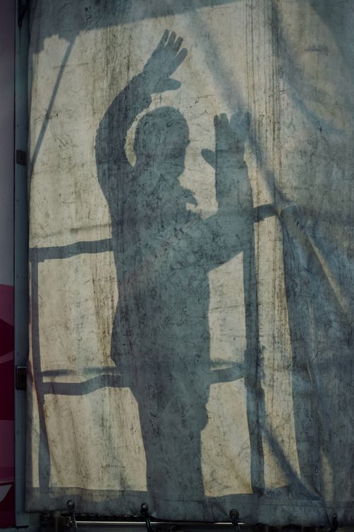 Free Shadow of a person raising hands behind a translucent canvas creating a mysterious effect. Stock Photo