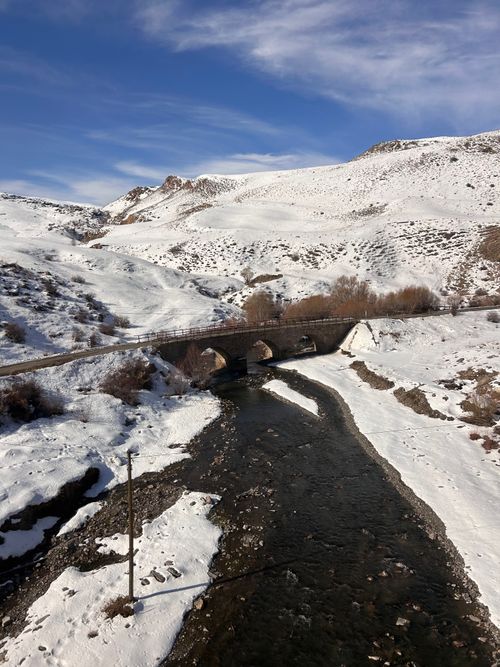Free Winter scene of a snow-covered valley with a stone bridge over a flowing river. Stock Photo