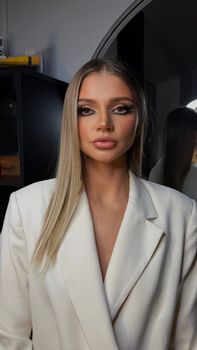 Portrait of a woman with stylish makeup and white blazer, indoors.