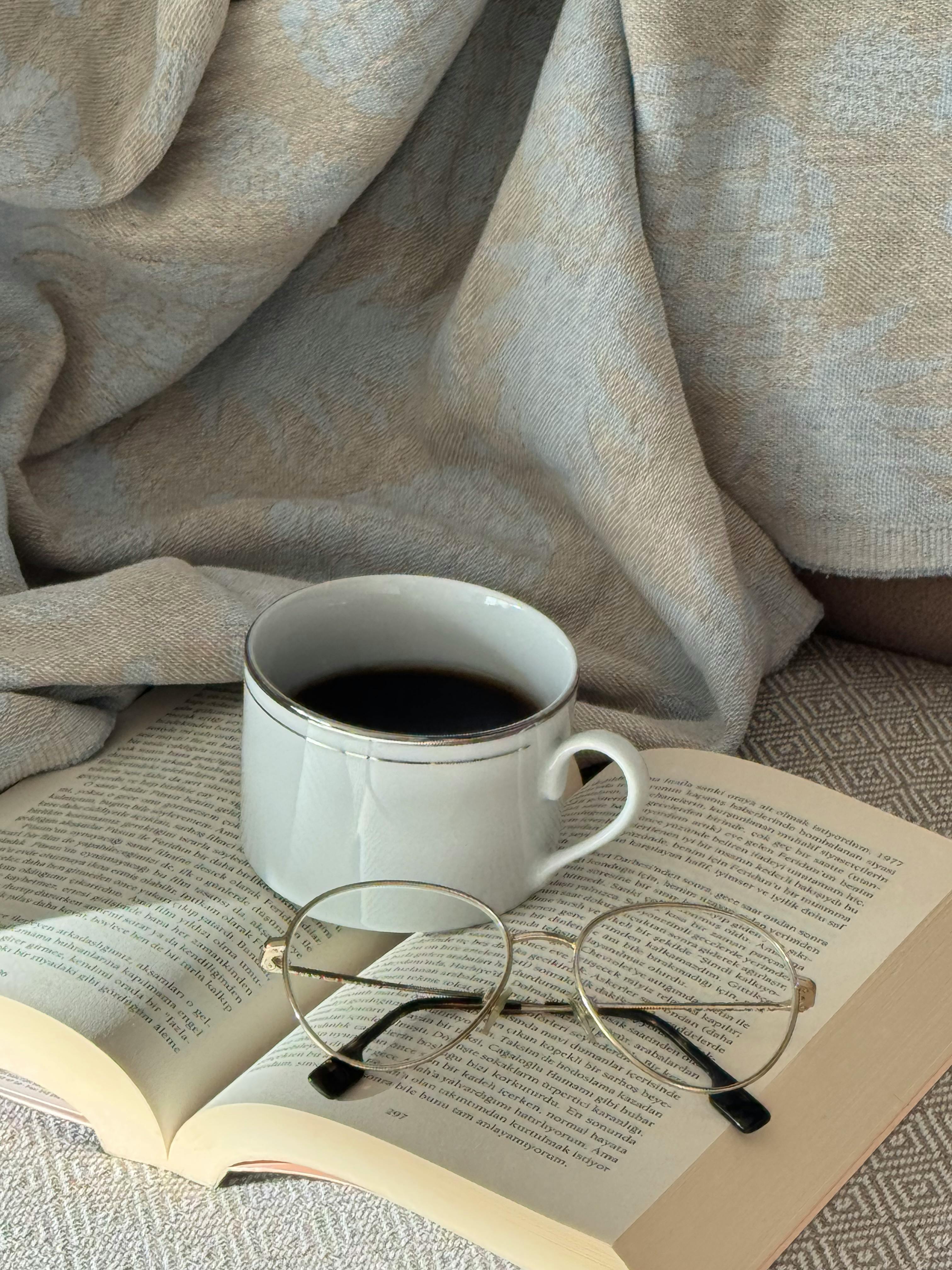 無料 心地よい雰囲気を醸し出す、一杯のコーヒー、開いた本、老眼鏡を配した落ち着いたシーン。 写真素材