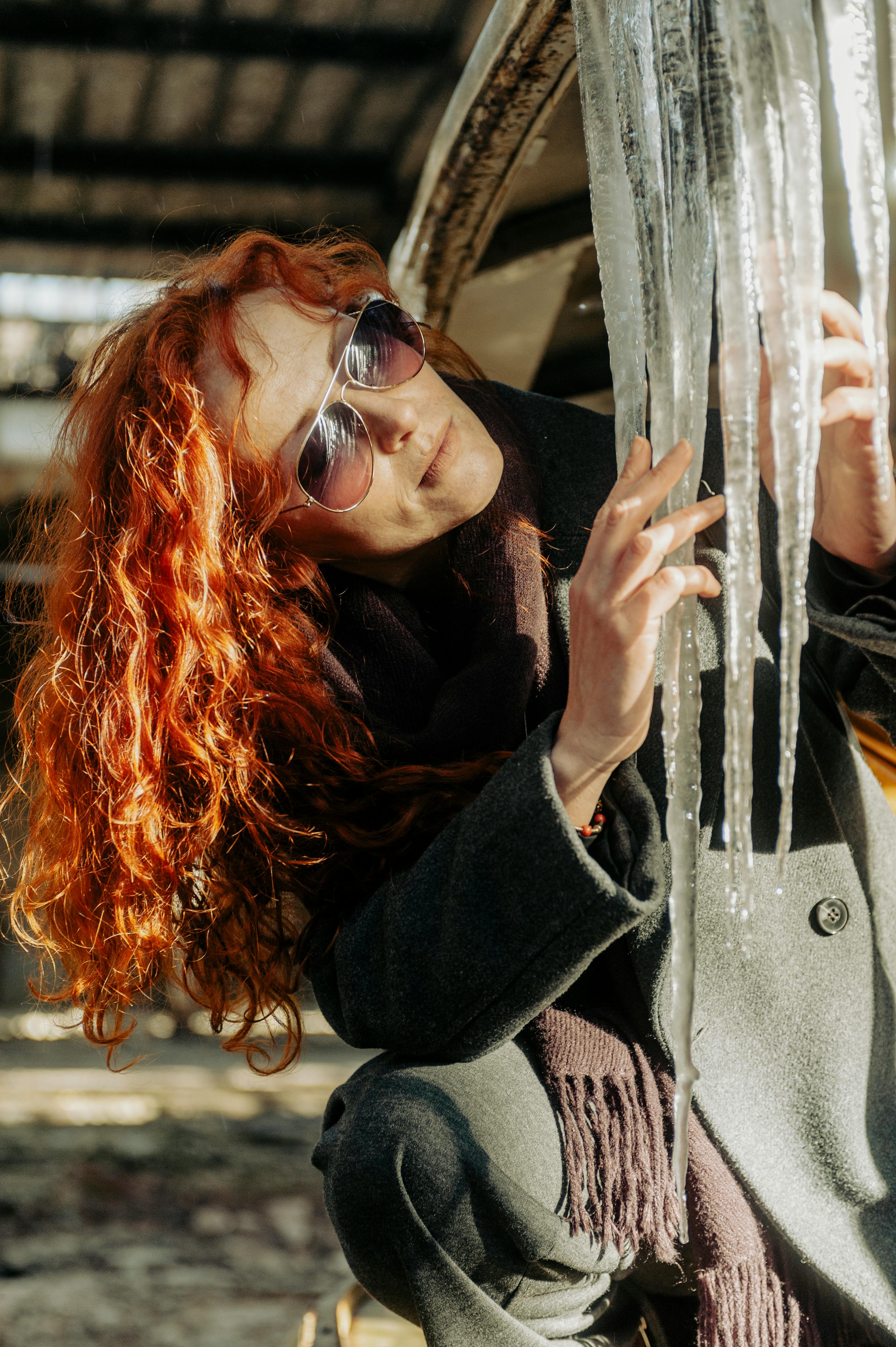 Free A stylish woman with red hair examines large icicles in an urban setting in Lviv, creating a vibrant winter scene. Stock Photo