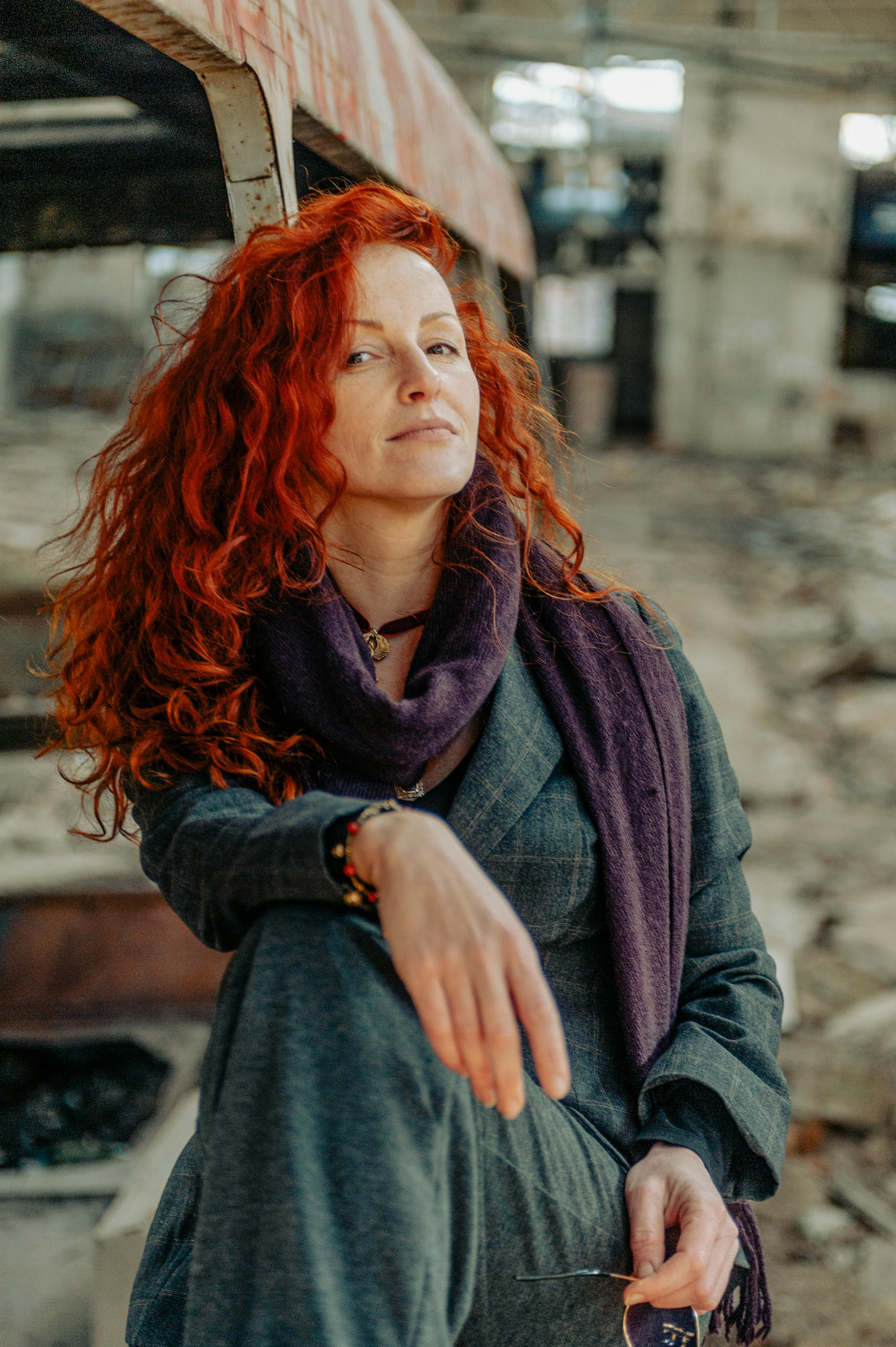 Confident woman with red hair sitting in an abandoned industrial setting. Urban exploration vibes.