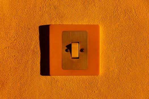 Close-up of a yellow light switch on a textured wall, highlighting minimalism.