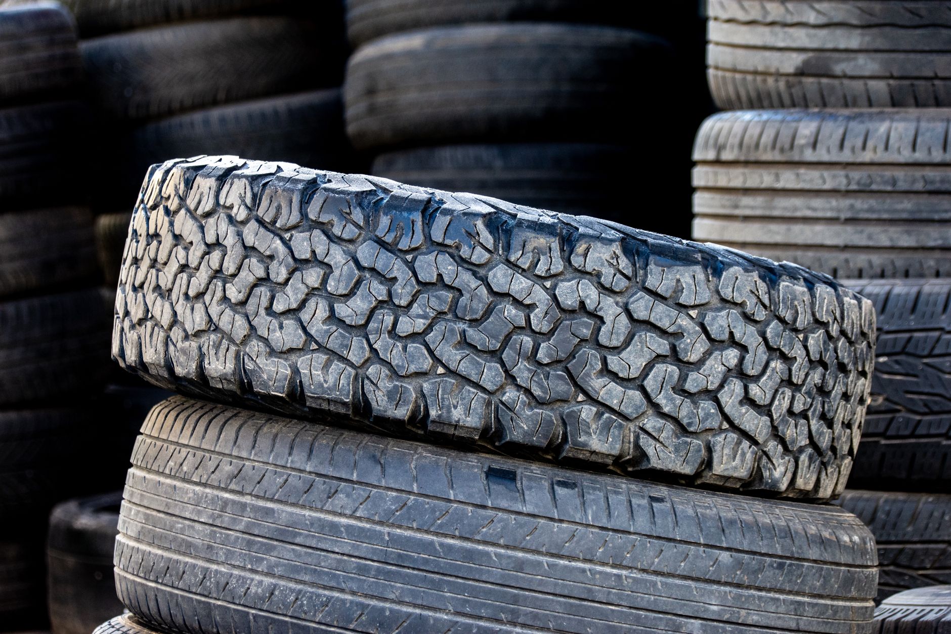 Close-up of stacked automotive tires showcasing rugged tread patterns in an outdoor setting.