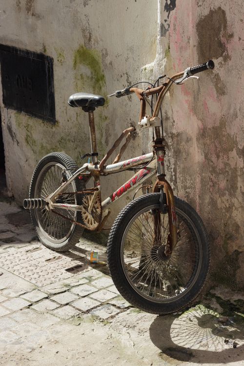 Free A rusty vintage bicycle against an aged wall with sunlight casting shadows. Stock Photo