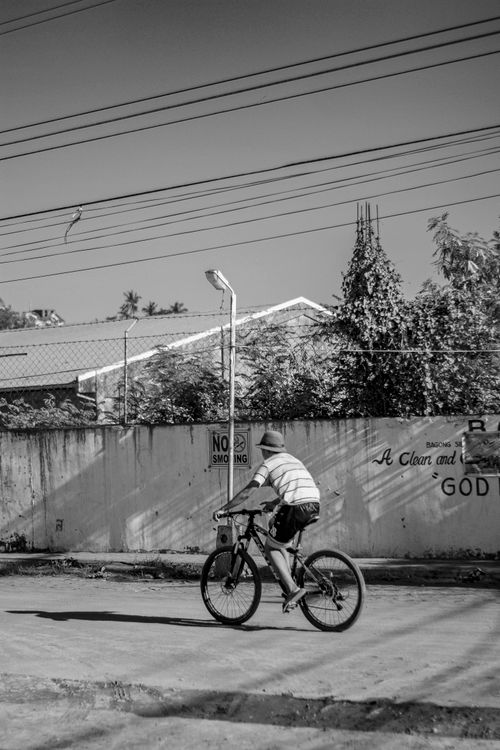Free Black and white of unrecognizable young guy in casual clothes and hat riding bicycle on road near residential house on sunny day in countryside Stock Photo