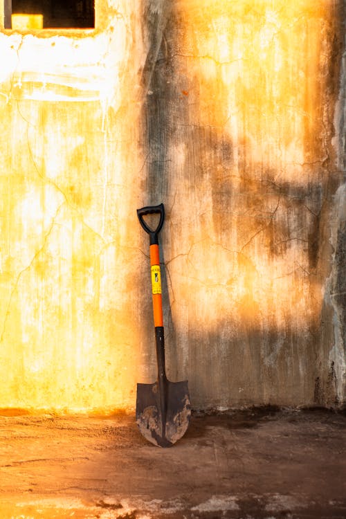 Dirty metal shovel leaned on shabby wall of old house during renovation works on sunny day