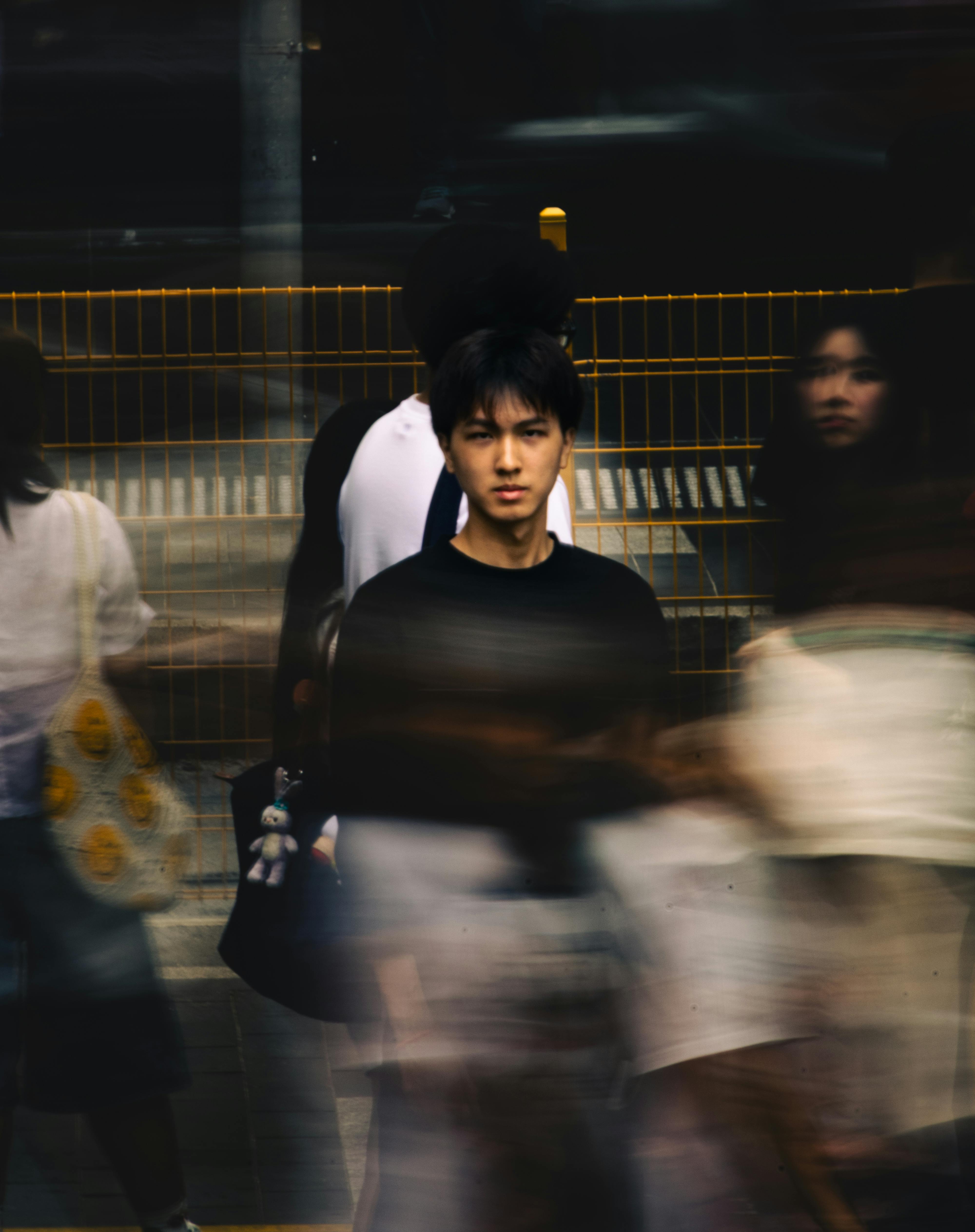 無料 メルボルンの賑やかな通りで、若いアジア人男性がモーションブラーの中でじっと立っている。 写真素材