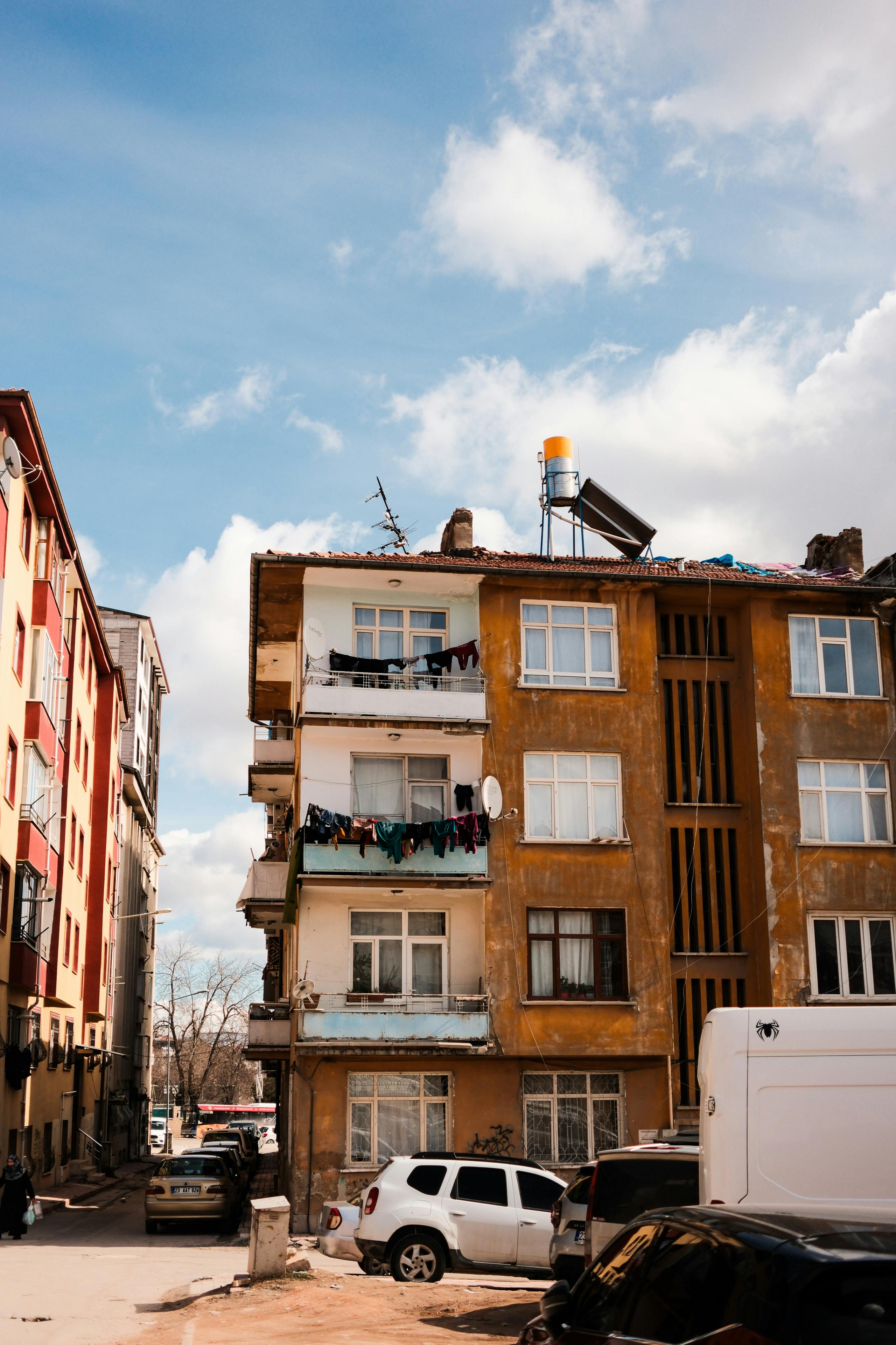 無料 澄み切った青空を背景に、バルコニーとその下に駐車された車がある 4 階建ての都市型アパート。 写真素材