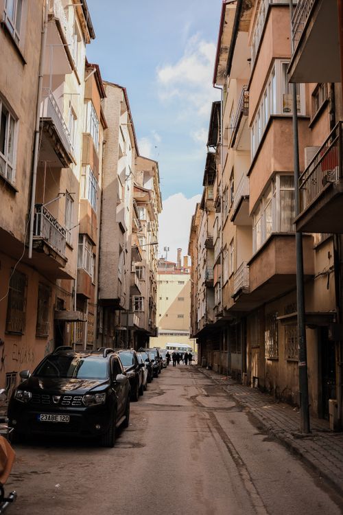 Free View of a narrow urban street lined with parked cars and apartment buildings under a blue sky. Stock Photo