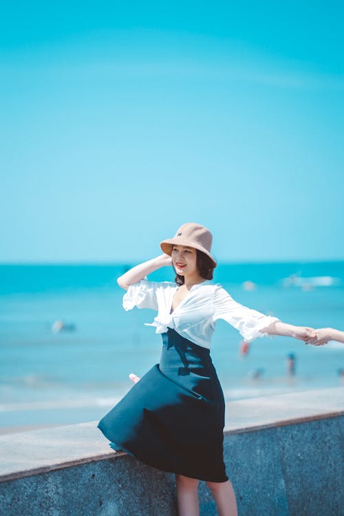 Woman in White Long Sleeve Shirt and Black Skirt Wearing White Hat Standing on Seaside · Free Stock Photo Woman In White Long Sleeve Shirt And Black Skirt Wearing White Hat Standing On Seaside · Free Stock Photo
