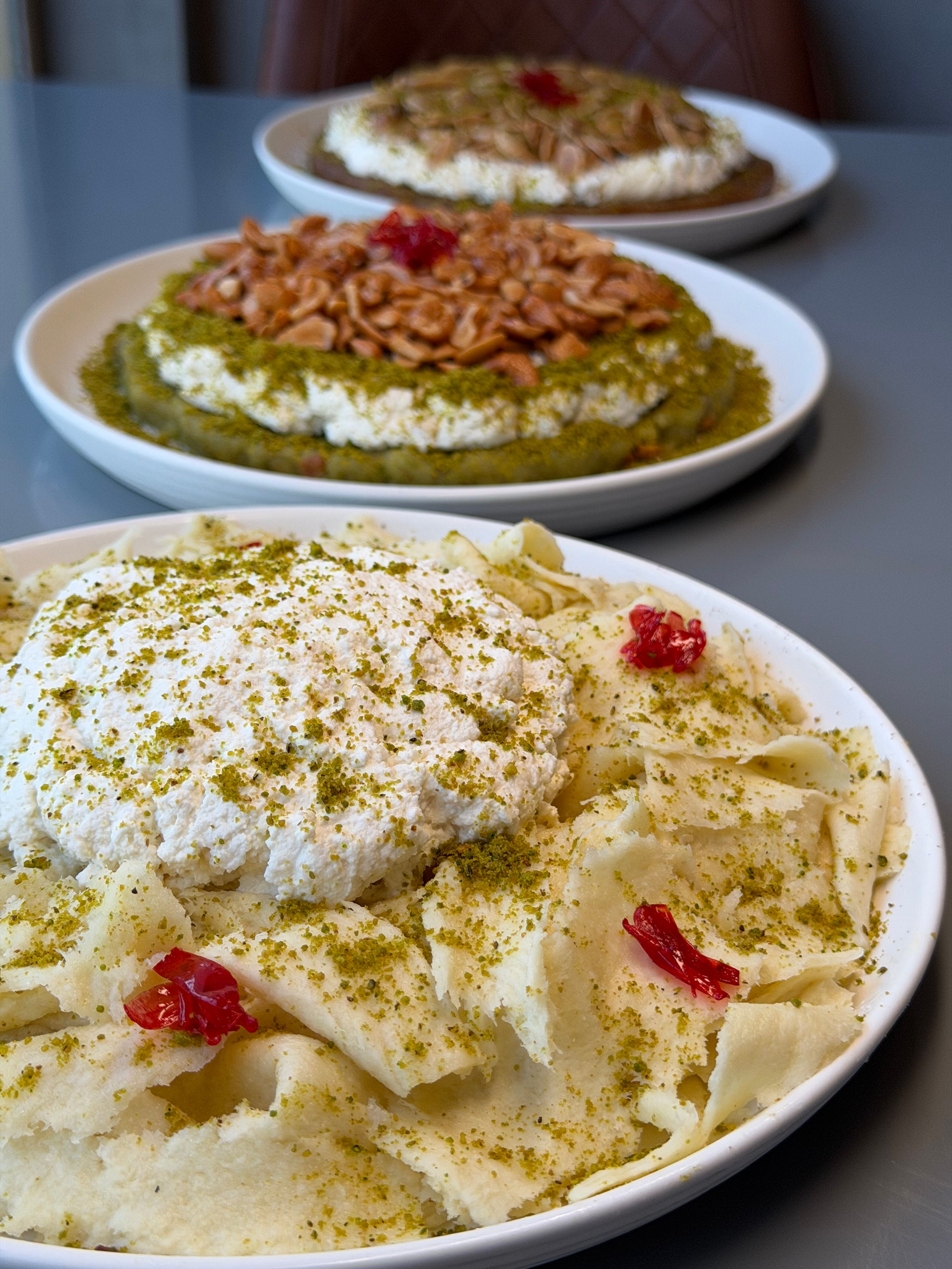 Close-up of traditional Middle Eastern desserts topped with cream and nuts on a table.