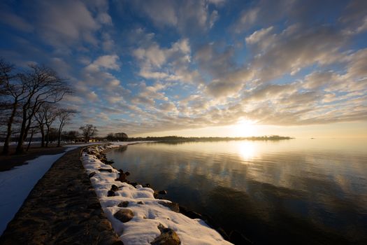 Beautiful winter sunrise over the calm waters of Stamford's Cove Island Park, with snow-covered breakwall.