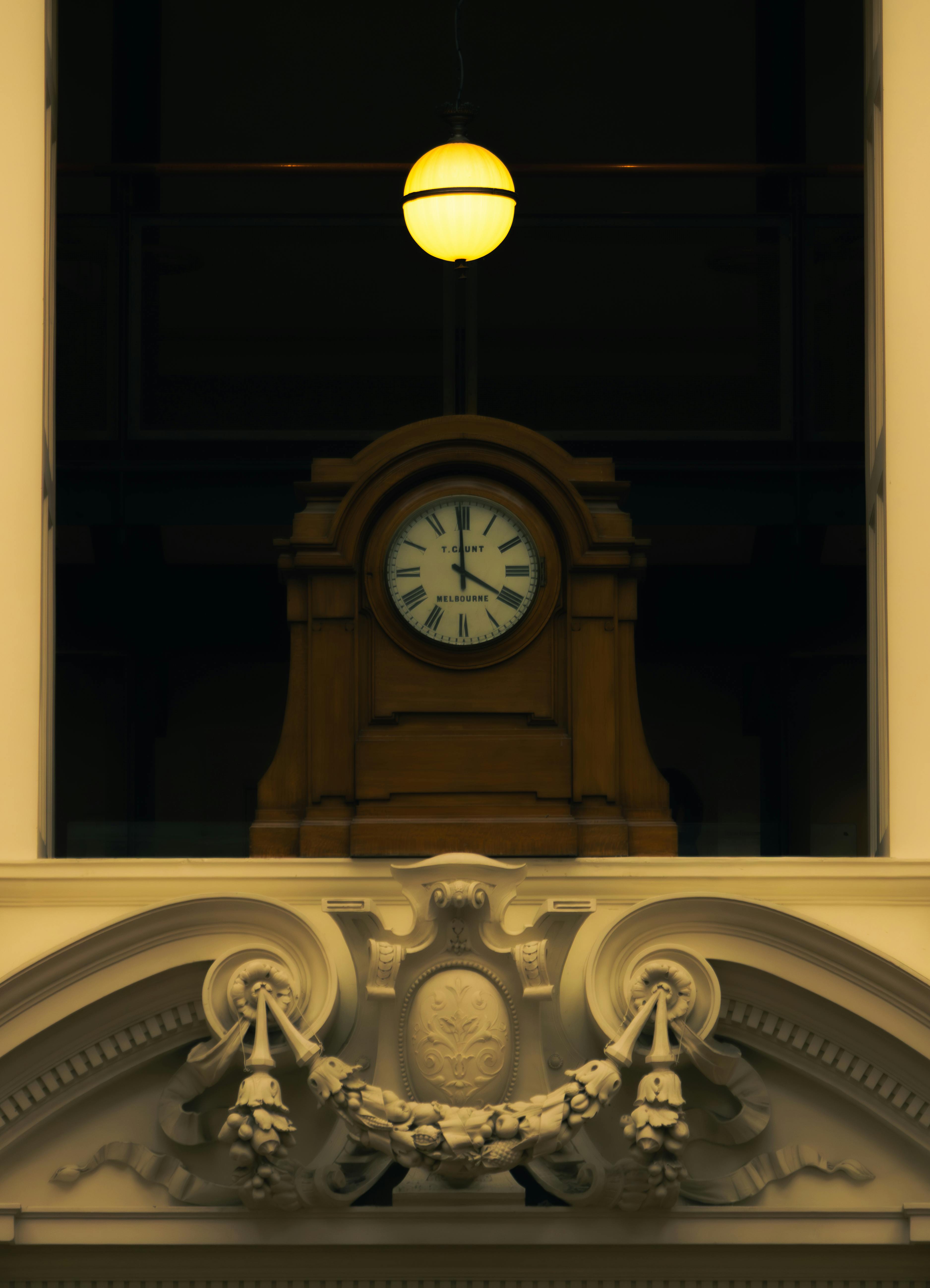 gratis Een antieke klok, omgeven door gedetailleerde Victoriaanse architectuur met warme verlichting. Stockfoto