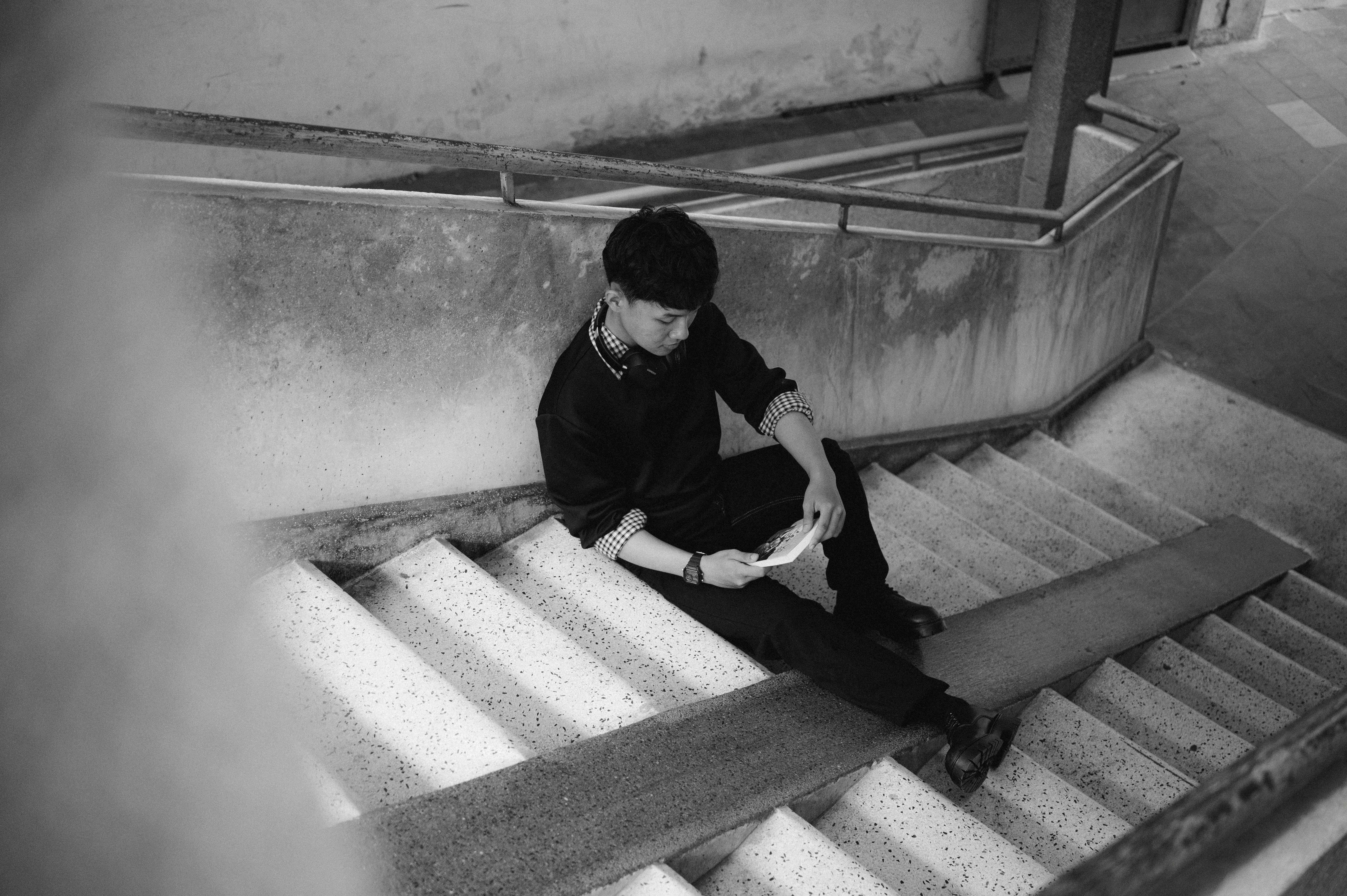 Free Young adult man sitting on stairs in an urban setting, engrossed in thought. Stock Photo