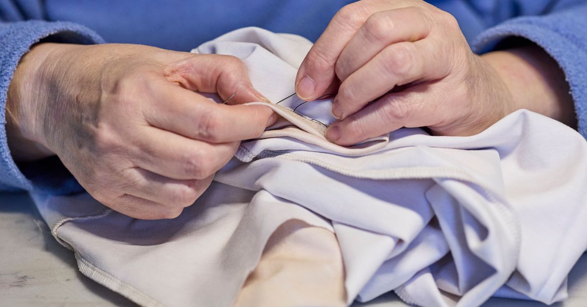 A close-up of hands mending a colorful sock with visible stitching, or repairing a ceramic mug with gold lacquer