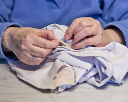 Detailed image of hands sewing white fabric, showcasing precision and skill in a traditional craft.