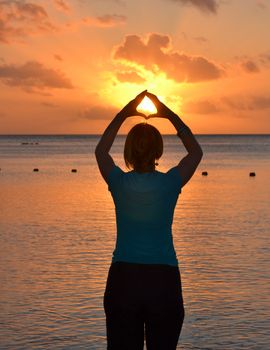 Woman in silhouette performing yoga pose by the ocean during a beautiful sunset.