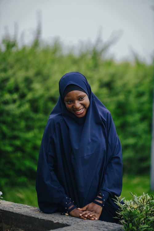 Free Portrait of a smiling woman wearing a hijab in a lush green outdoor setting. Stock Photo