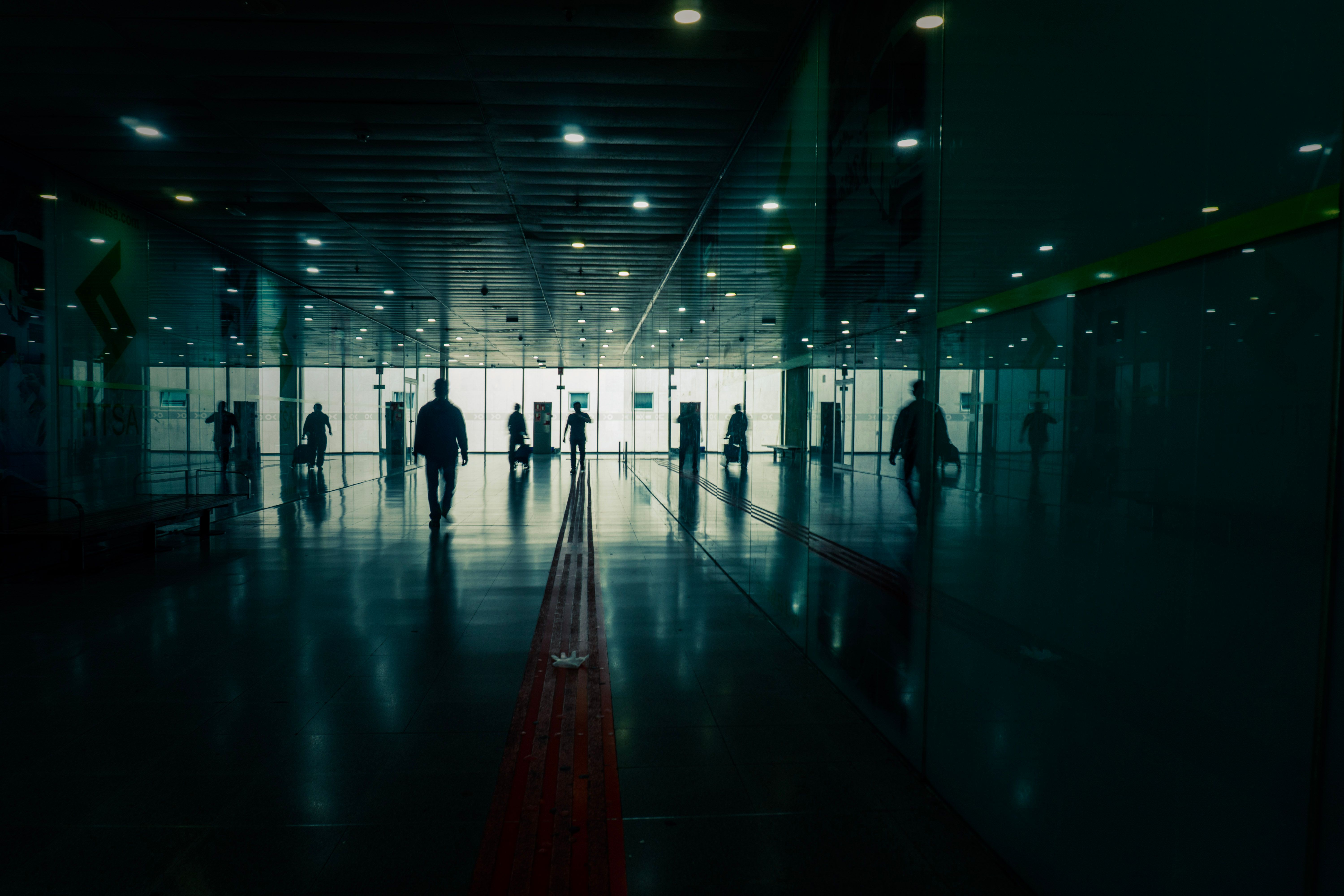 Silhouettes in a modern terminal creating a moody atmosphere with reflections on the floor.