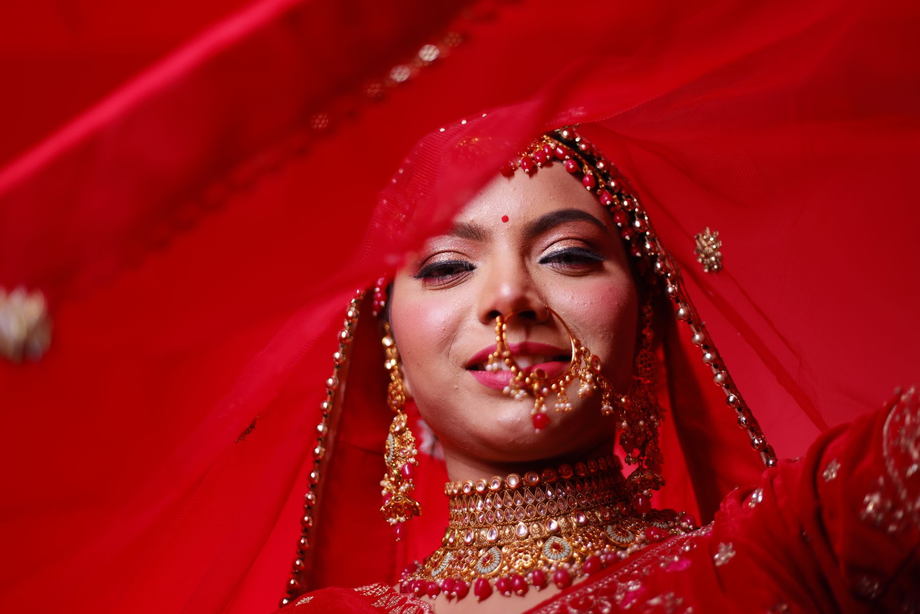 Close-up of a beautiful Indian bride in vibrant red attire, showcasing traditional jewelry.