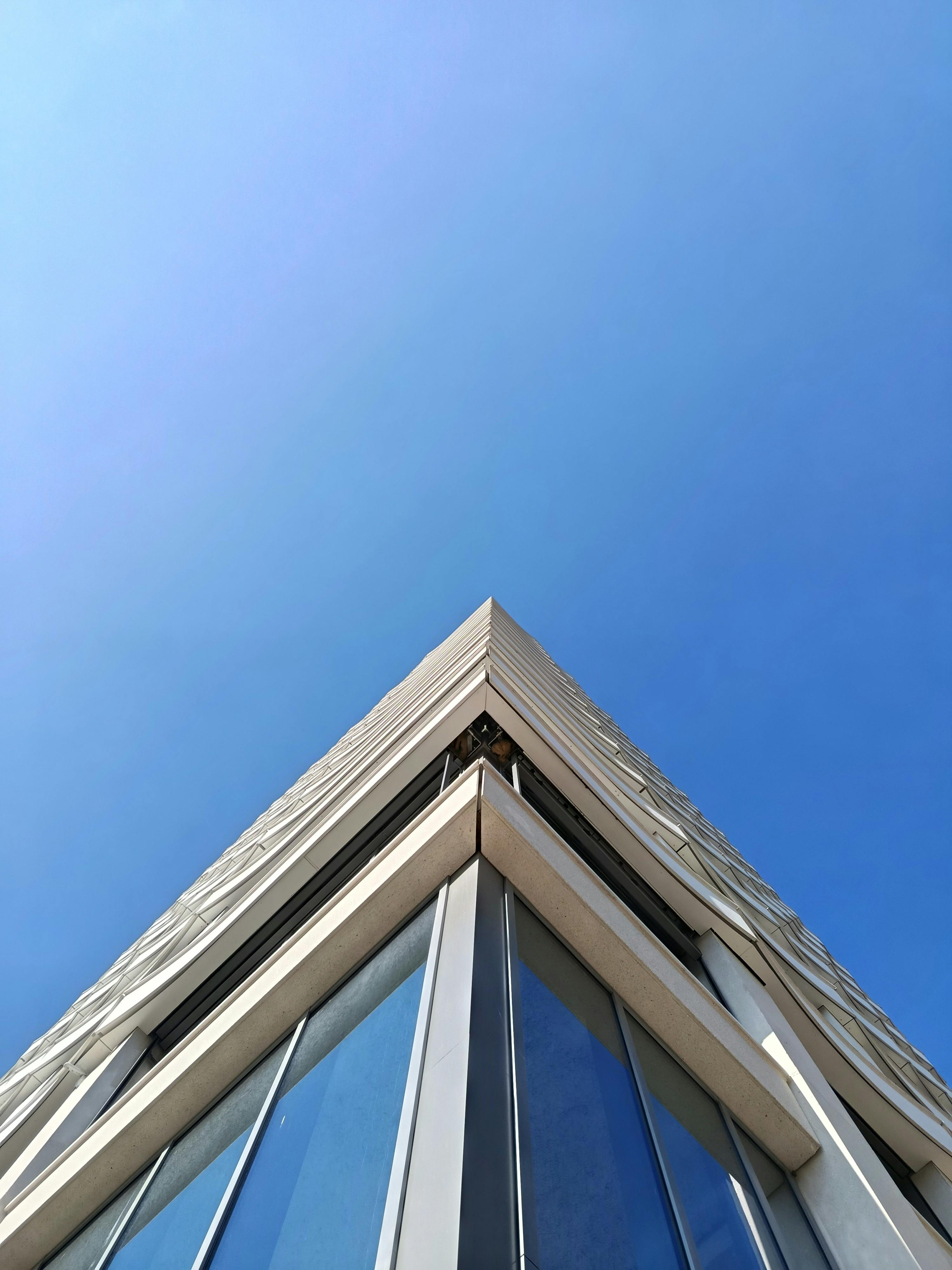 Kostenlos Moderne Wolkenkratzerfassade mit Glasfenstern vor strahlend blauem Himmel. Ansicht aus der Froschperspektive. Stock-Foto