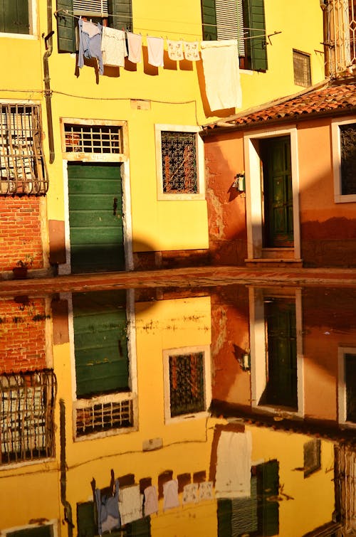 Bright yellow wall of old house and clothes on string reflecting in puddle