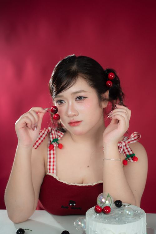 Free Young woman posing with cherry-themed accessories against a red background. Stock Photo