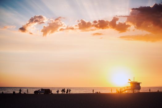 Silhouetted people enjoy a beach sunset next to a lifeguard tower and ocean view.