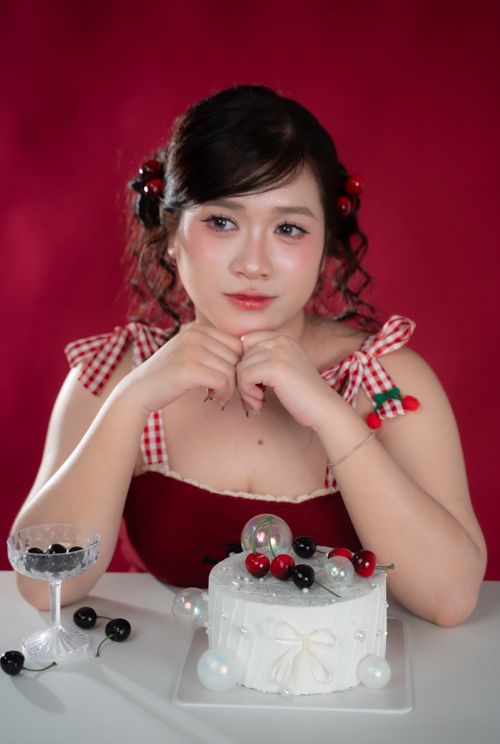Free Charming woman posing with a decorated cake and cherries in a vibrant red setting. Stock Photo