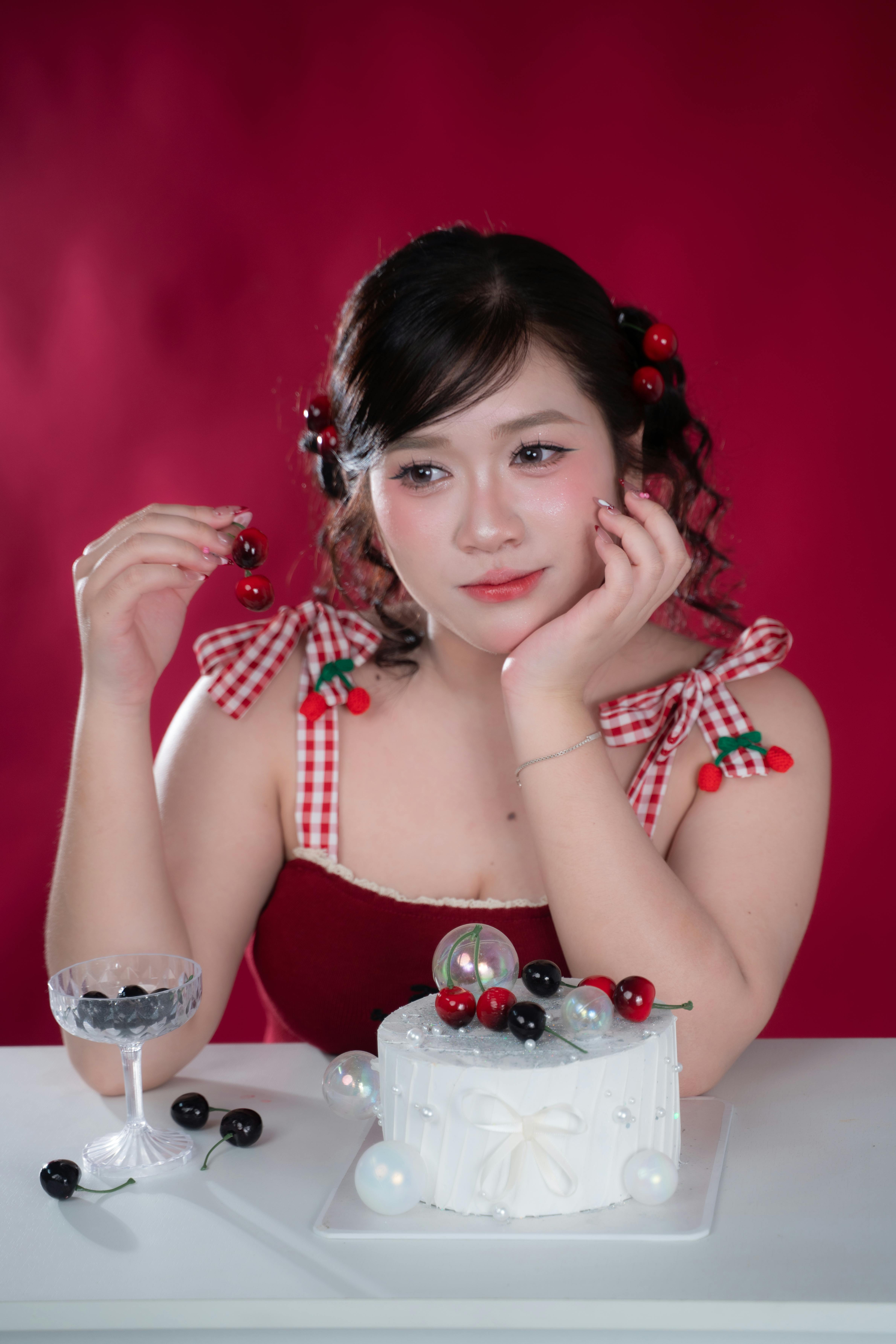 無料 チェリーで飾られたケーキの横に立つ赤いドレスを着た大人の女性 写真素材