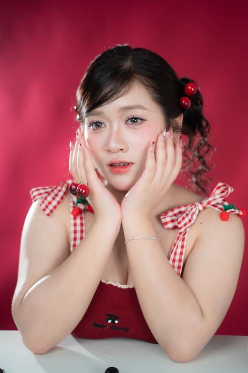 Free Portrait of a woman with cherry-themed accessories against a red backdrop, evoking a playful and stylish mood. Stock Photo