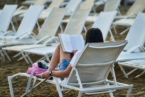 Vrouw Die In Blauwe Denimborrels Op Wit Het Boek Van De Lezingslezing Van De Stoel Zitten