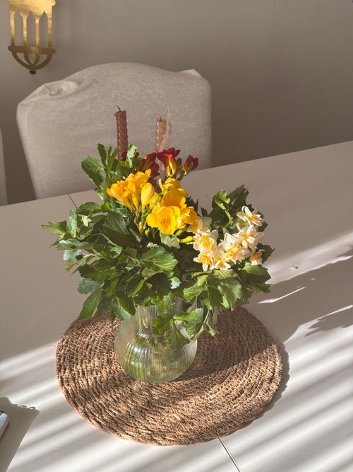 Free Colorful bouquet of yellow and white flowers in a glass vase on a woven mat. Stock Photo