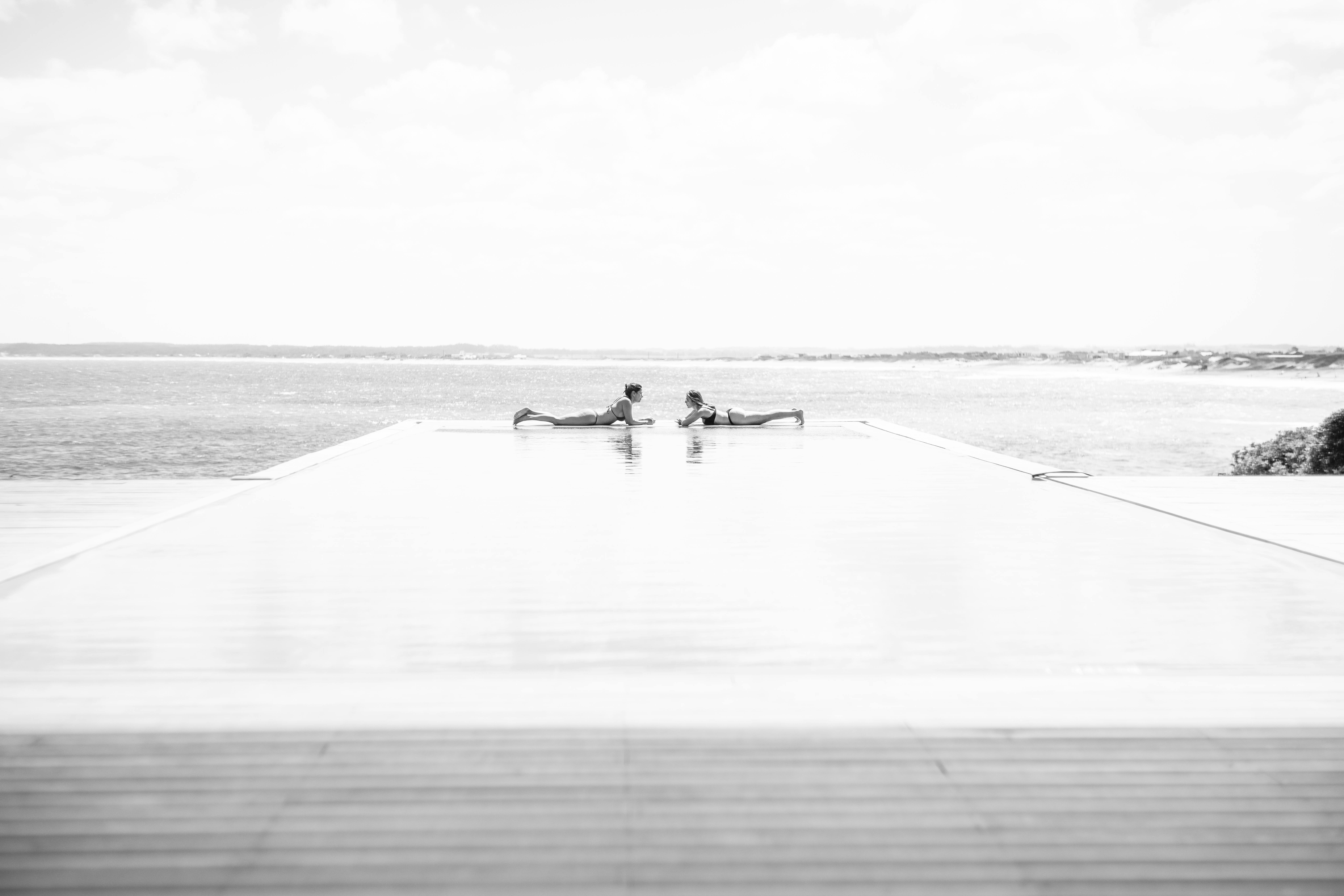 Free Serene scene at an infinity pool with two women relaxing, ocean in view. Stock Photo