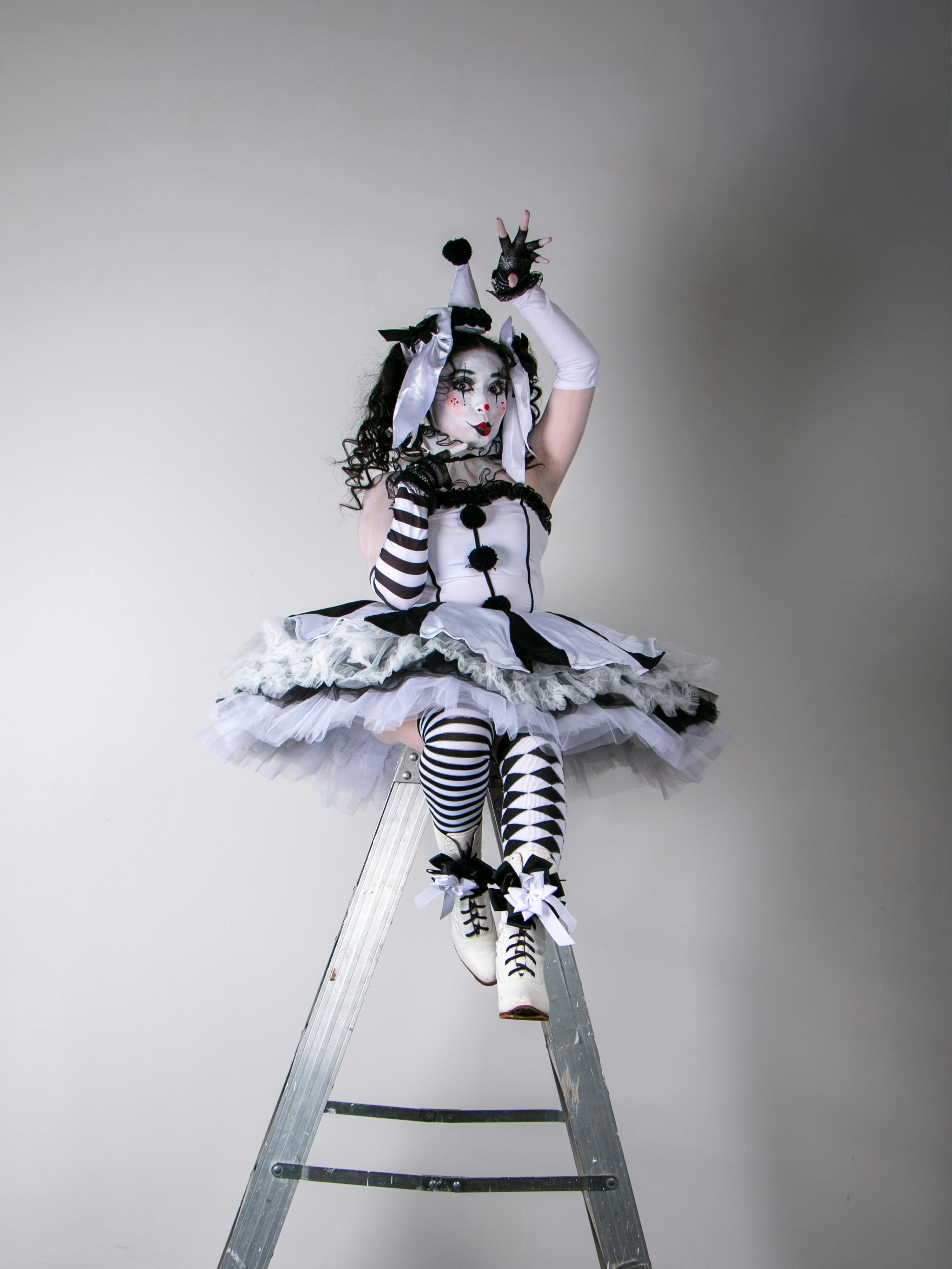 Ücretsiz Siyah beyaz soytarı kostümü giymiş, hayal gücü yüksek bir kadın palyaço, merdiven üzerinde sanatsal bir şekilde oturuyor. Stok Fotoğraflar