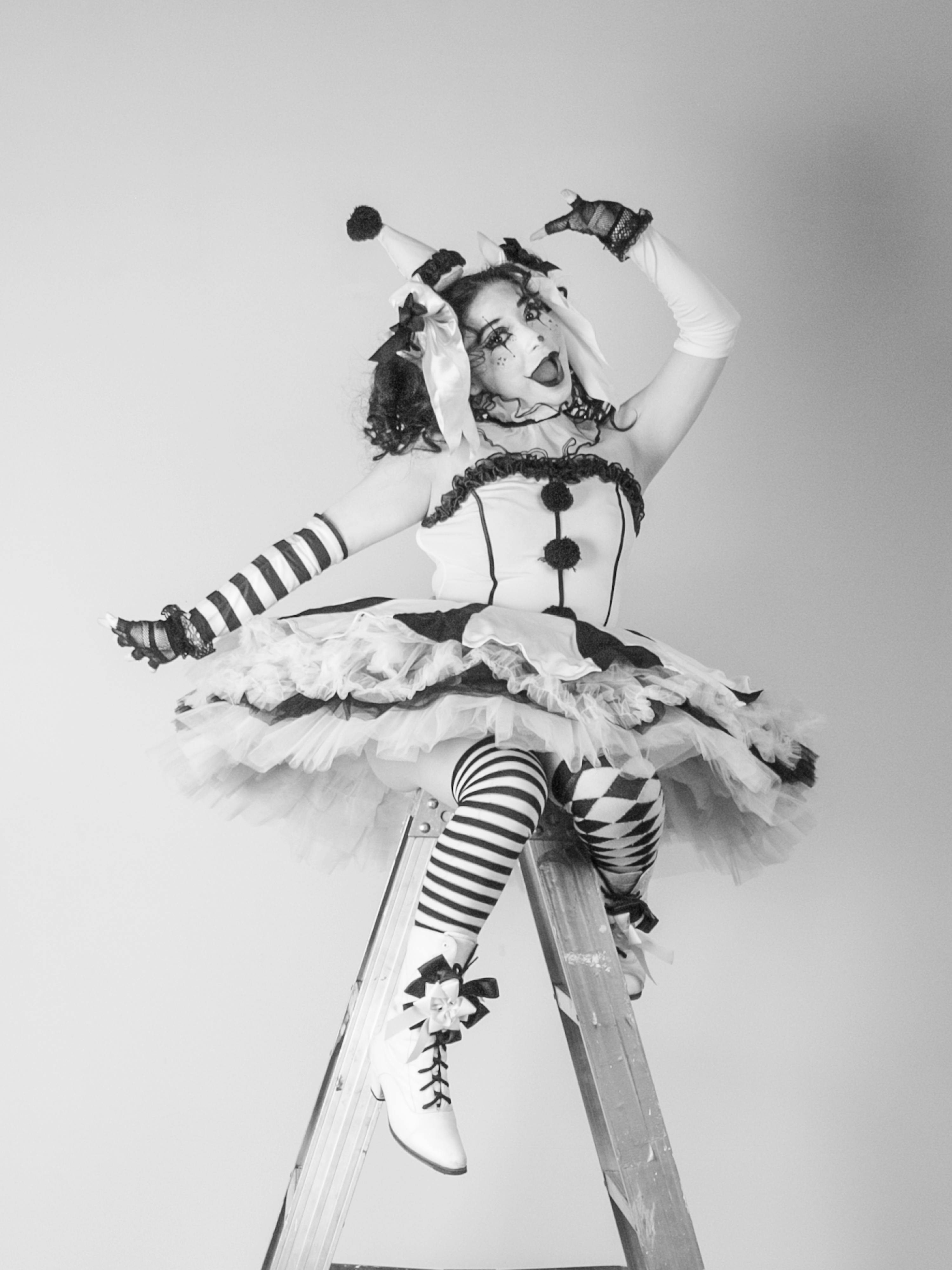 Gratis Una vivace donna adulta, vestita con un giocoso costume da clown, assume una posa bizzarra su una scala. Foto a disposizione