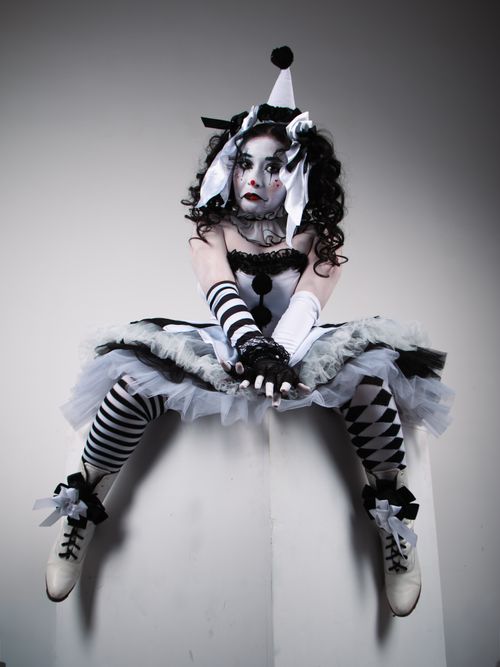 Free A dramatic harlequin dancer sits poised in striking monochrome costume against a neutral backdrop. Stock Photo