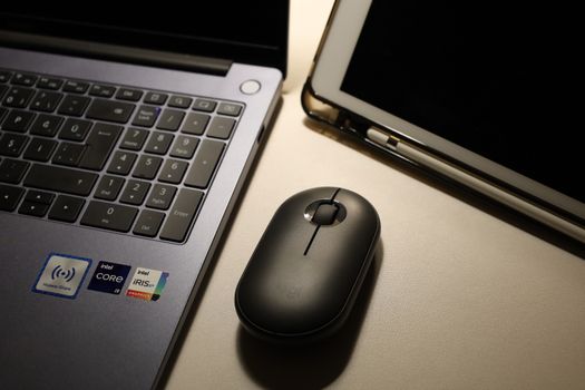 Close-up of a laptop, wireless mouse, and tablet on a desk, showcasing a modern workspace.