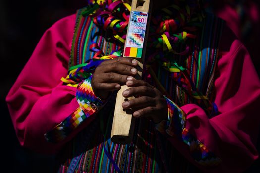 Close-up of hands holding a wooden flute during a vibrant cultural celebration in Chile.