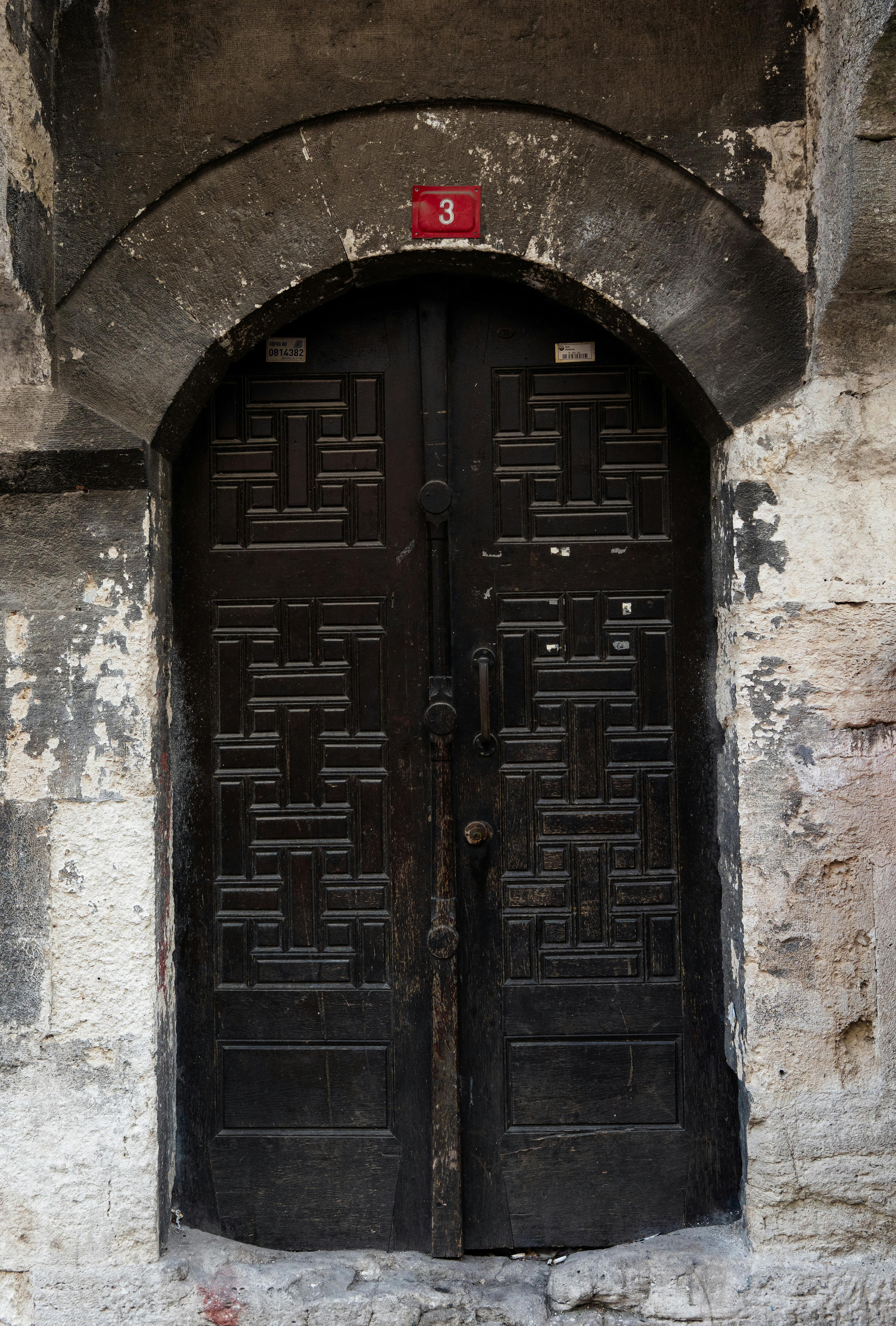 無料 石のアーチの下に、複雑なデザインが施された歴史的な木製のドアがあり、伝統的な建築様式を展示しています。 写真素材